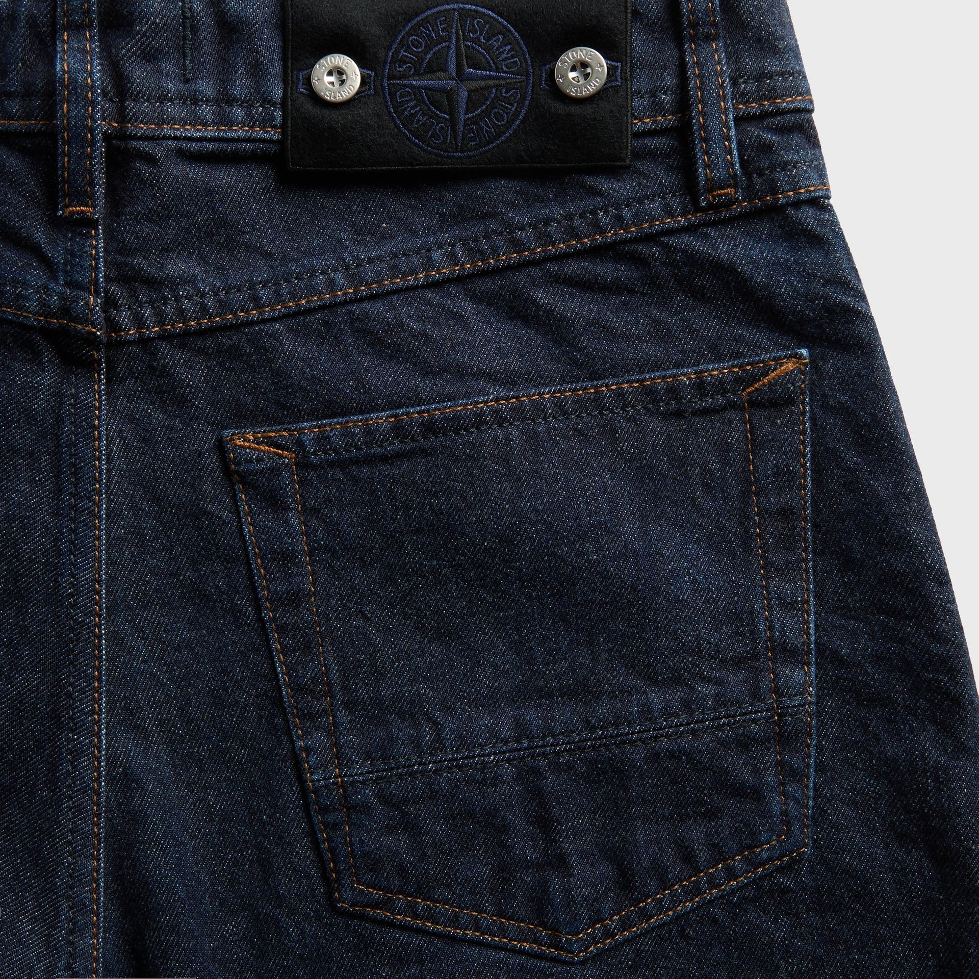 Detail of Stone Island navy-embroidered leather compass tab on rinsed indigo denim back pocket