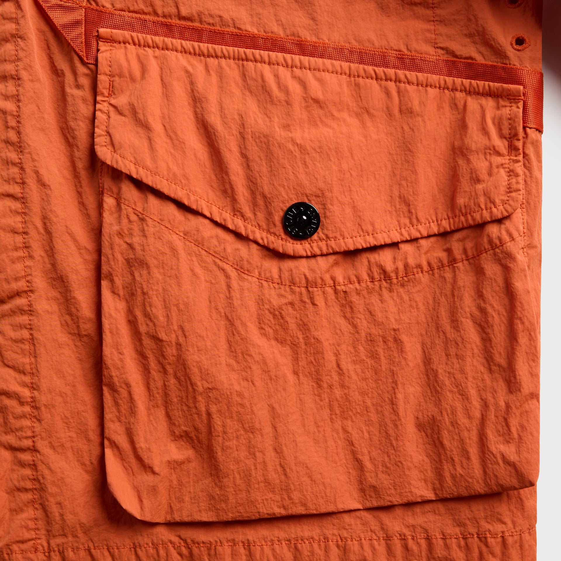 Close-up of burnt orange coach jacket flap cargo pocket with black snap button