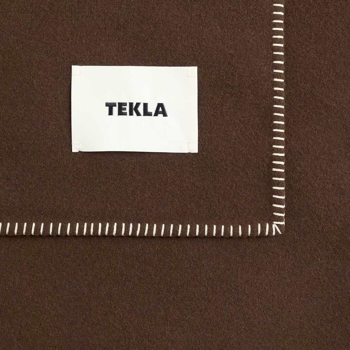 Tekla Lambswool Blanket in Walnut, close-up of corner with woven TEKLA label and whipstitched edge