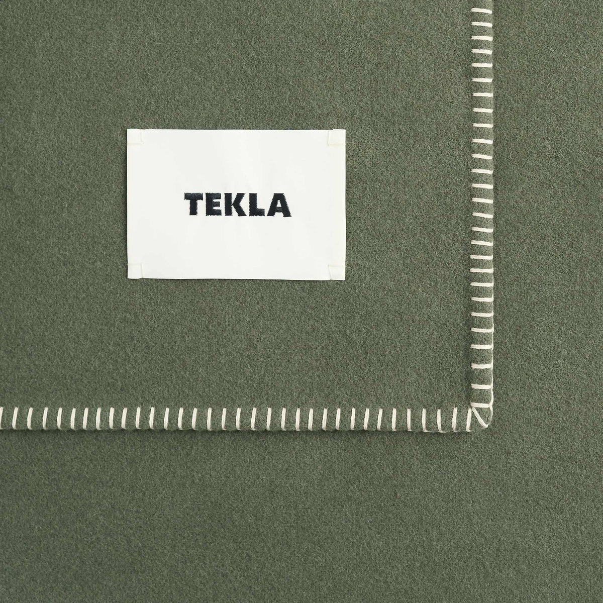 Tekla Lambswool Blanket in Willow, close-up of corner with woven TEKLA label and whipstitched edge