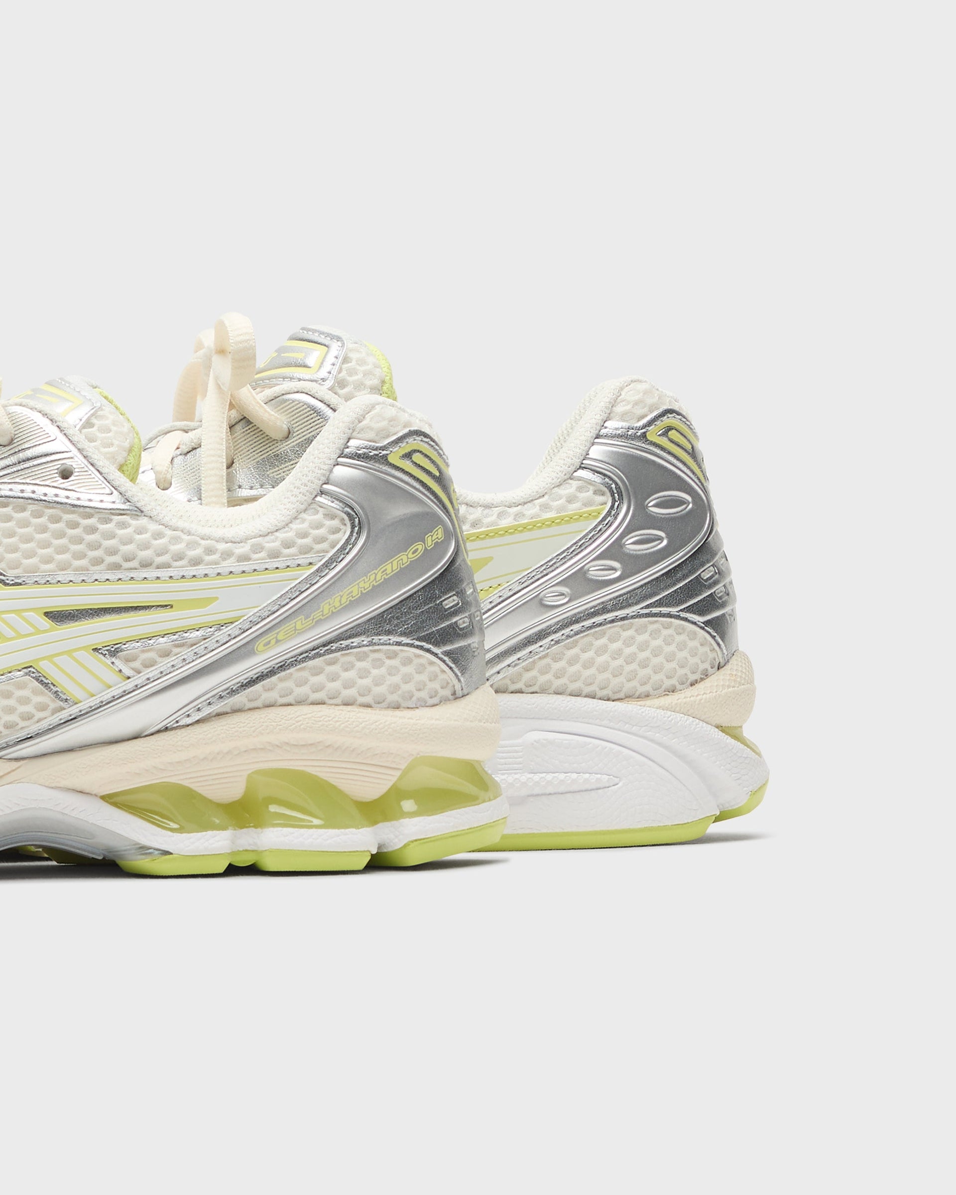 Asics Gel-Kayano 14 sneakers in cream and silver with lime green gel heel accents, rear three-quarter view of both shoes