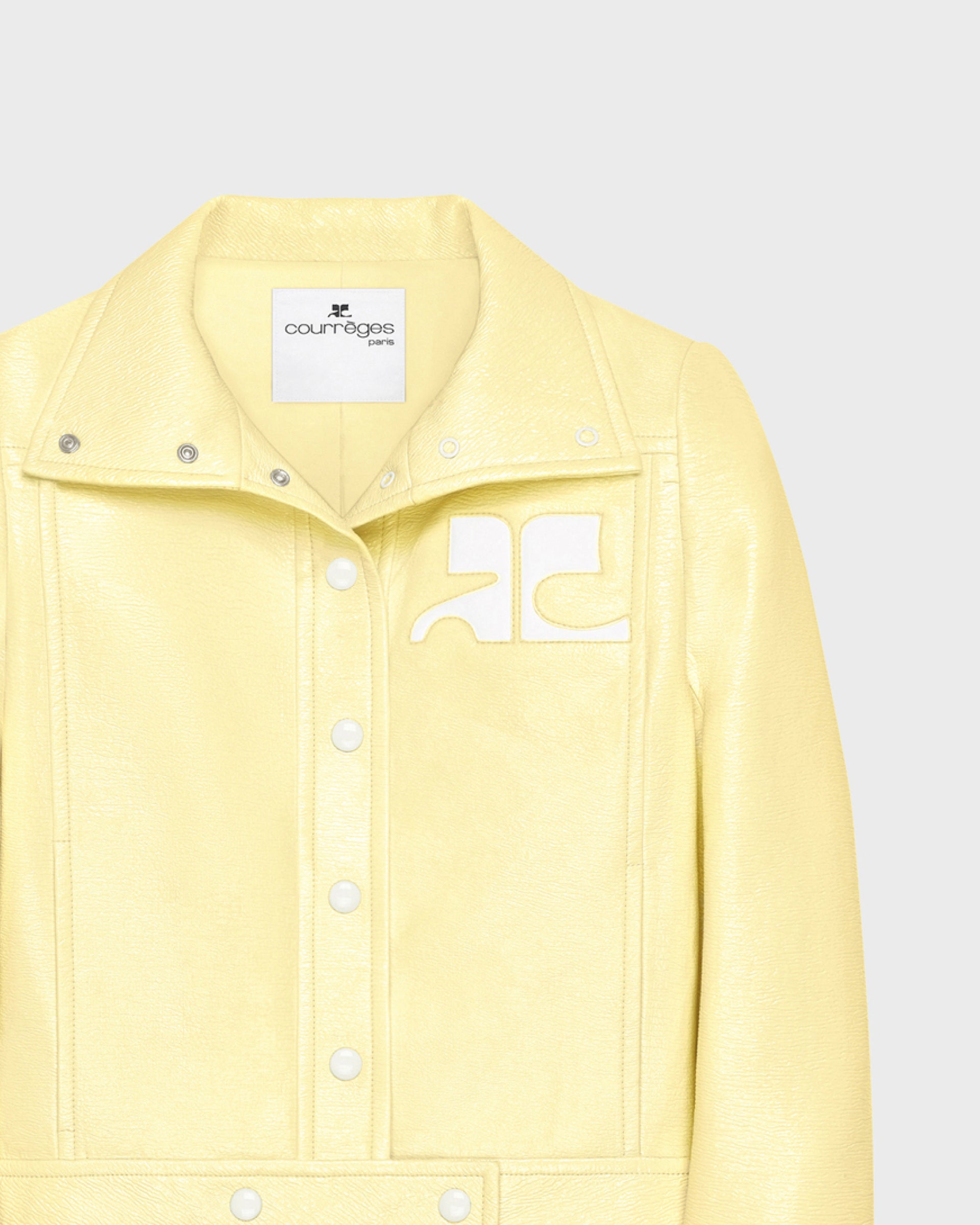 Courreges pale yellow patent leather jacket detail, snap-button placket and logo emblem on chest, close-up