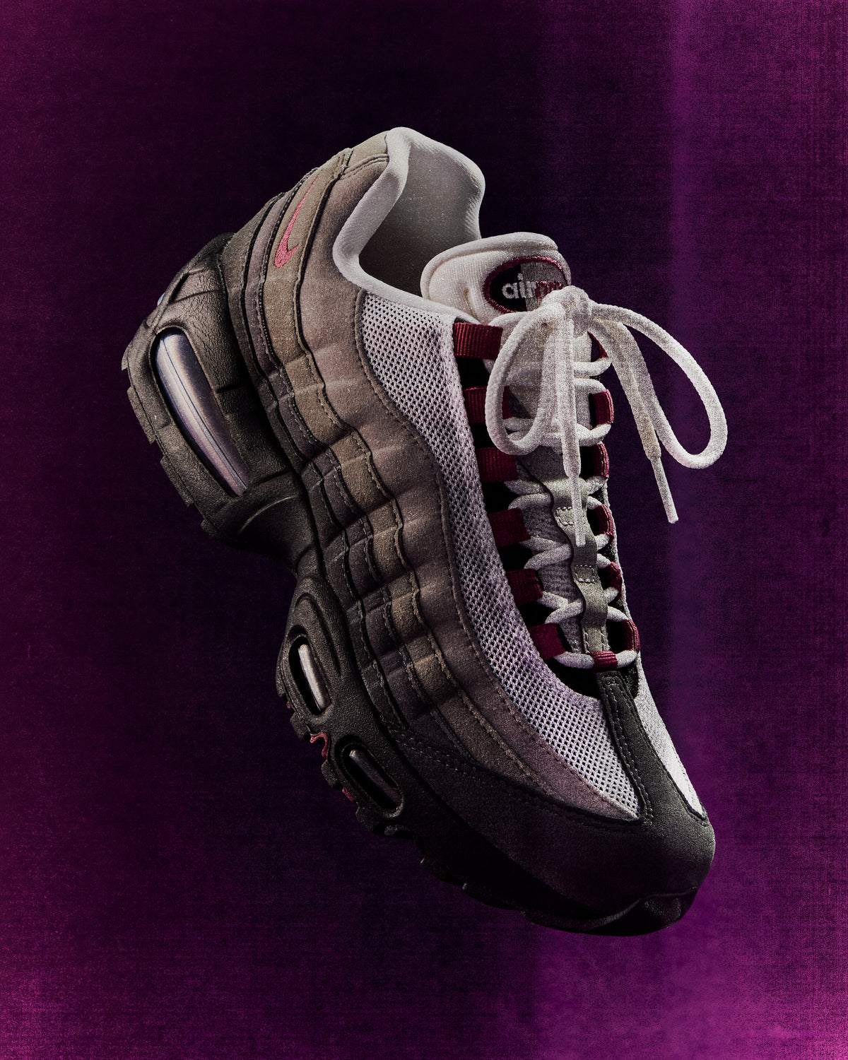 Nike Air Max 95 sneaker in grey gradient with burgundy accents and white laces, floating on a purple background