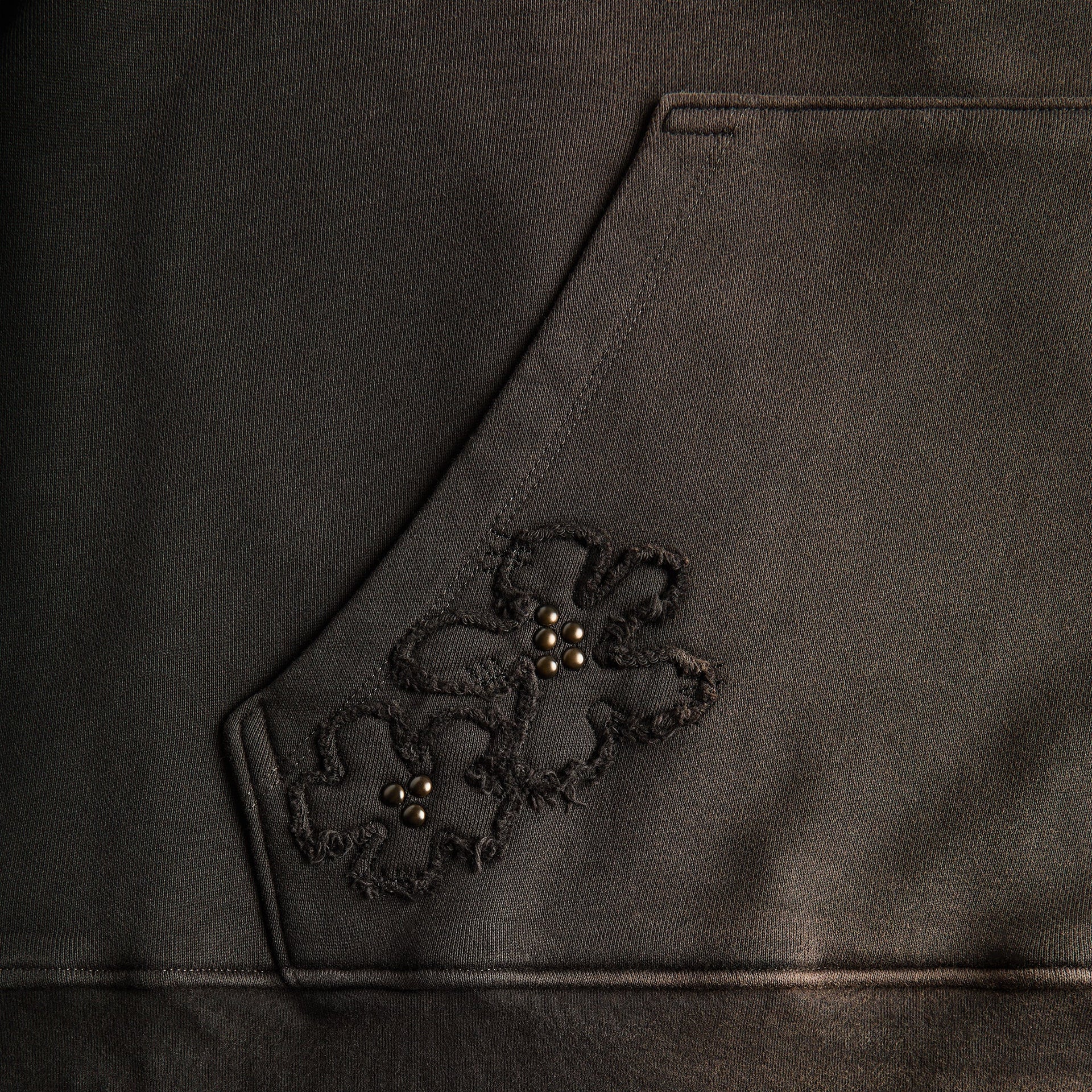 Close-up of NAHMIAS Flower Patch: black embroidered floral applique with beaded studded center on faded fabric