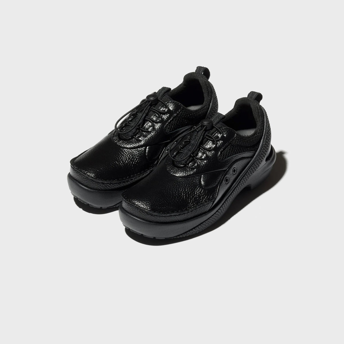 Crocs x Kiko Kostadinov VAALS in black, pair shown from front three-quarter angle with glossy pebbled leather and bungee laces